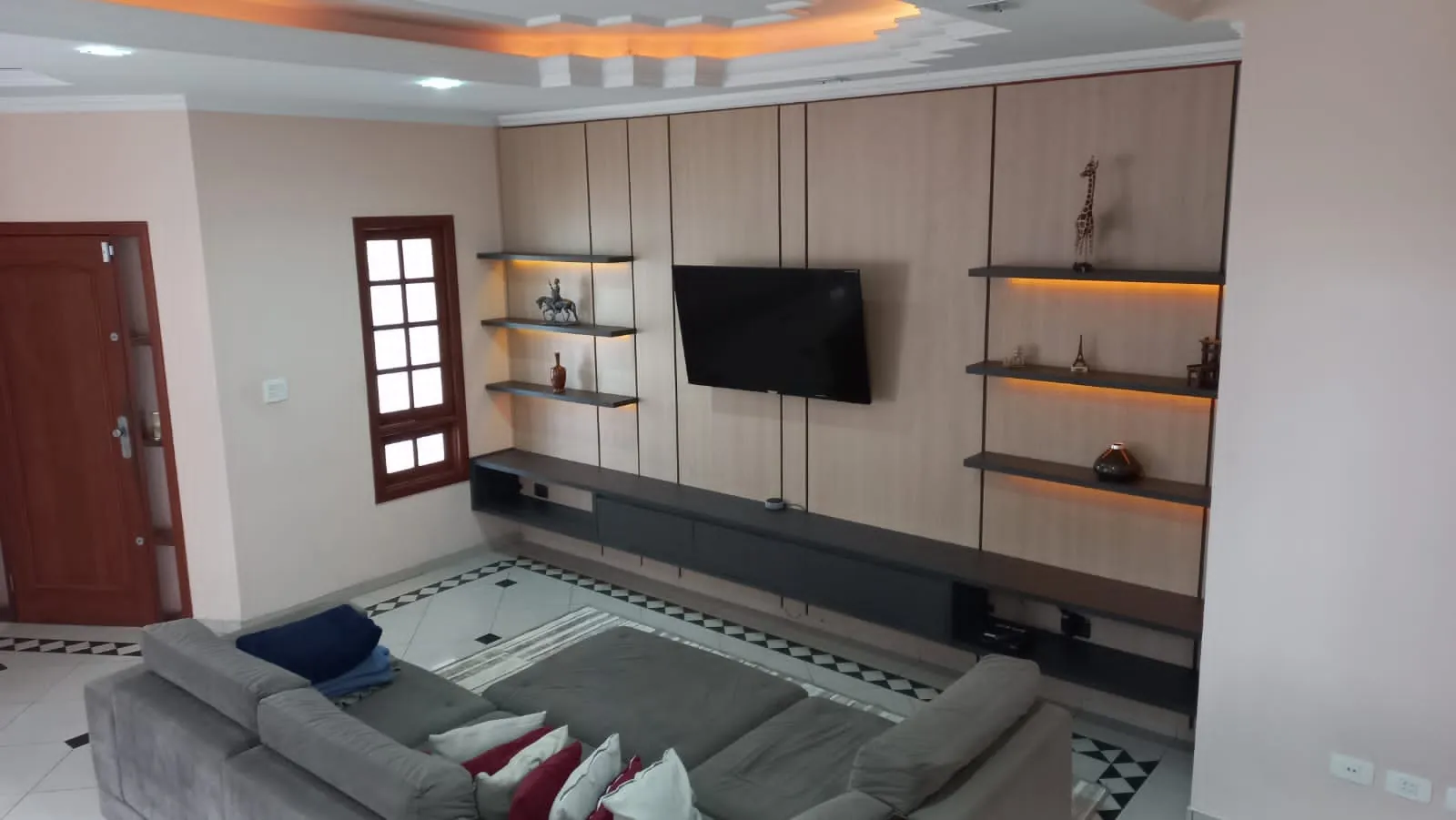 Sala com painel de madeira, nicho para televisão e prateleiras